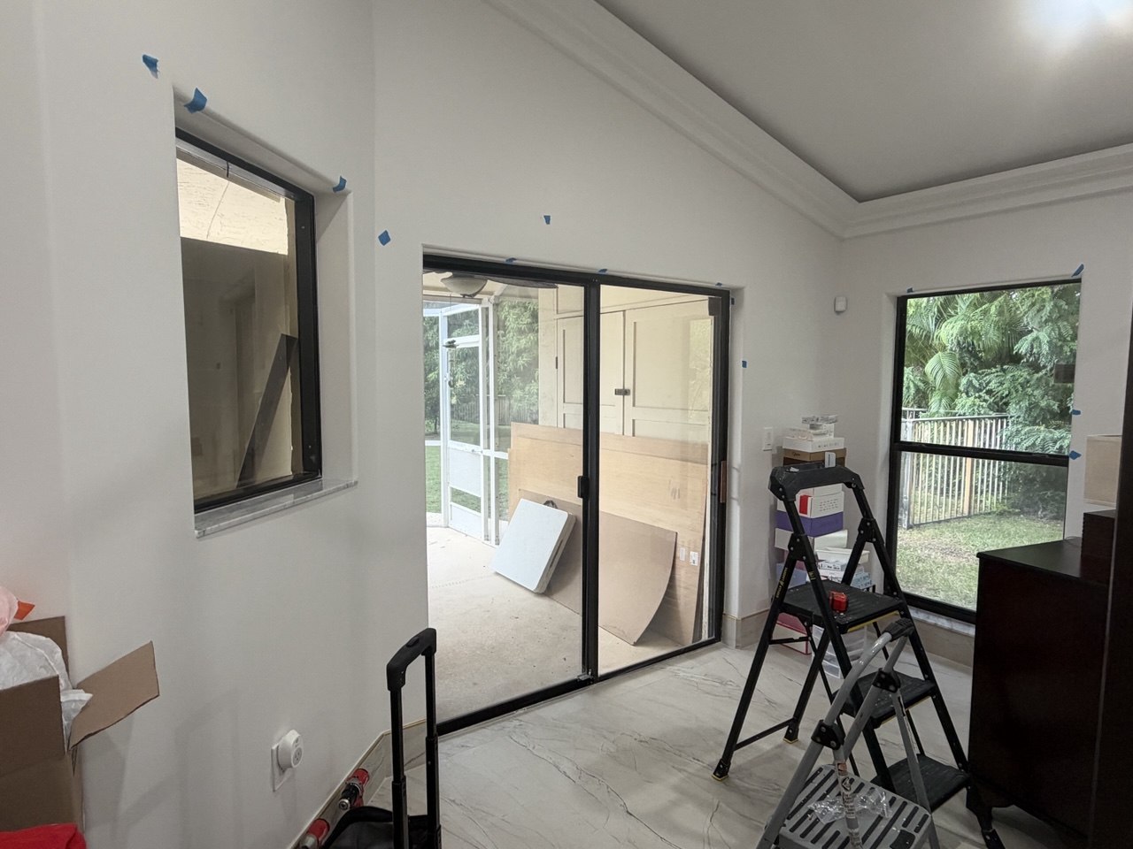 Uncovered bedroom windows and sliding glass door with ladders and preparation tape before zebra installation in Fort Lauderdale